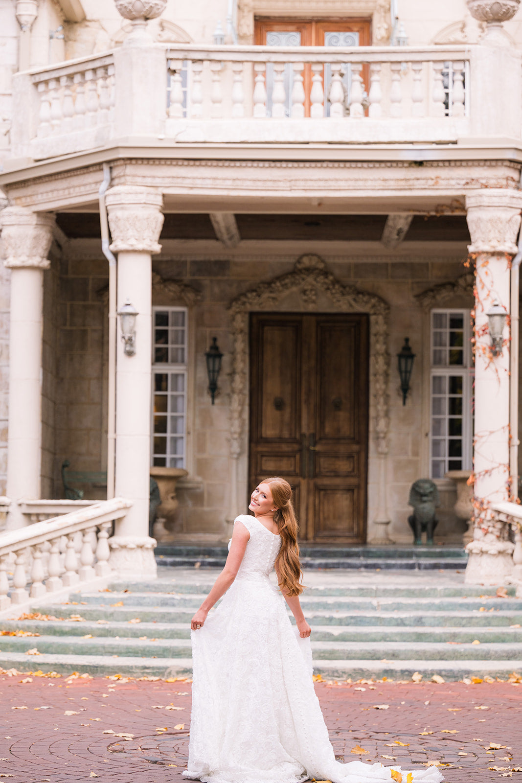 Woman in a white dress standing in front of a large, ornate building with columns and a wooden door.