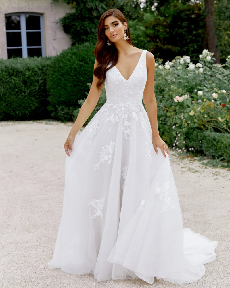Woman in a white wedding dress standing outdoors with greenery and a building in the background