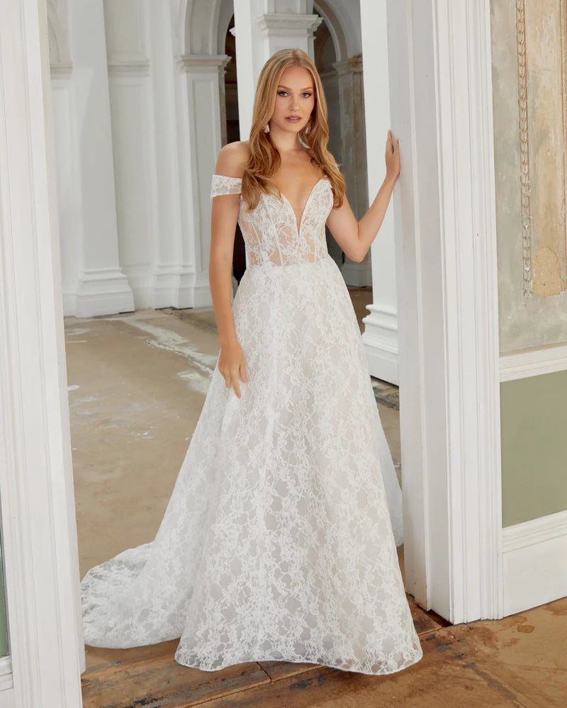 Woman in a white lace wedding dress standing in an elegant interior setting.