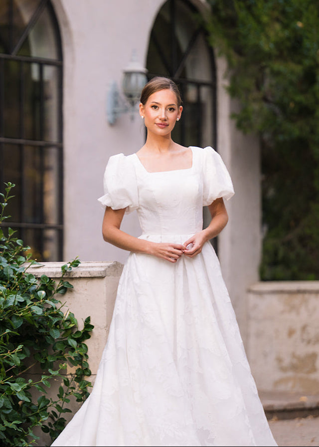 Woman in a white dress standing in front of a building with arched windows.