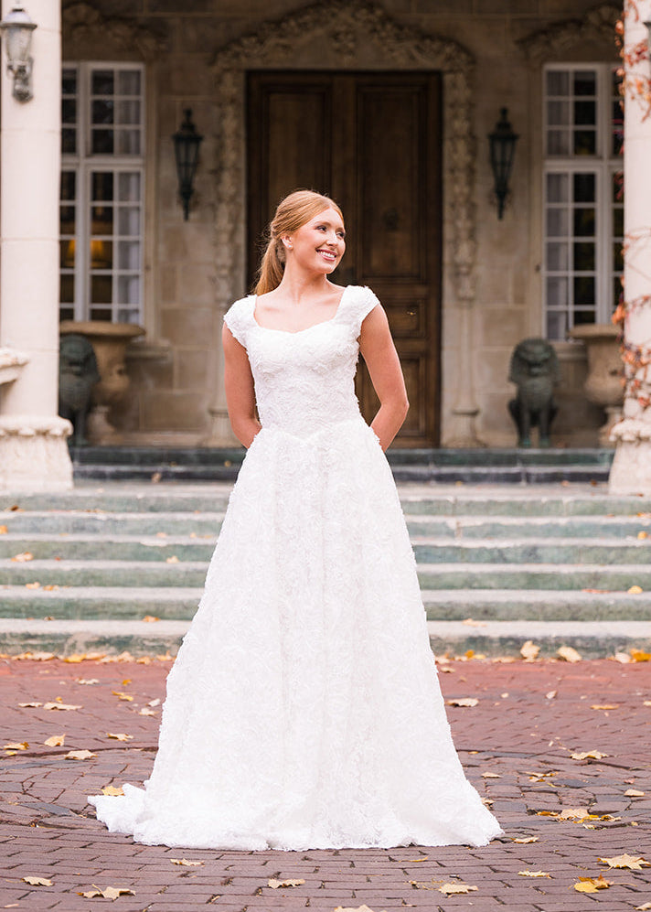 Woman in a white wedding dress standing in front of an elegant building with columns.