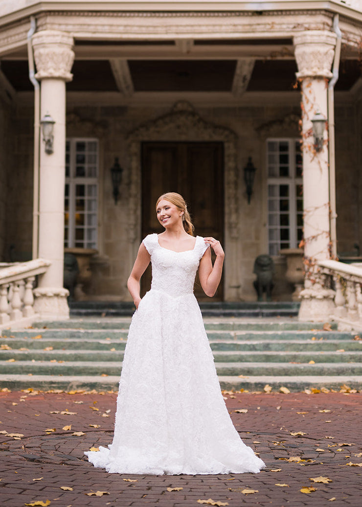 Woman in a white wedding dress standing in front of a large, ornate building.
