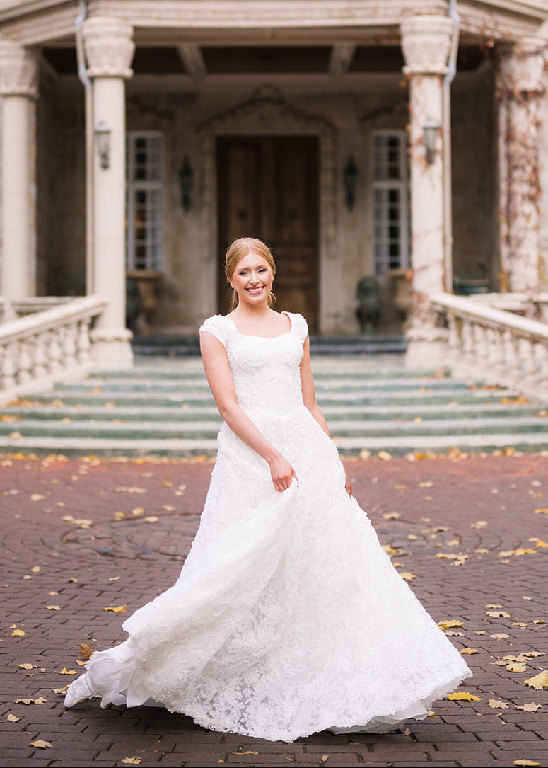 Woman in a white wedding dress standing in front of a large, elegant building with stone architecture.
