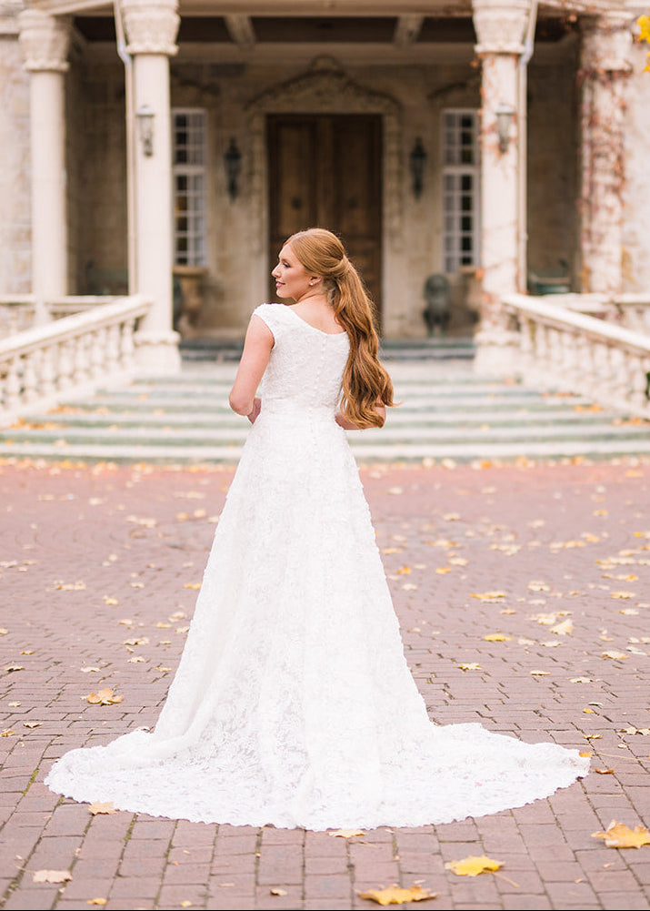 Woman in a white wedding dress standing in front of a large, elegant house with columns.