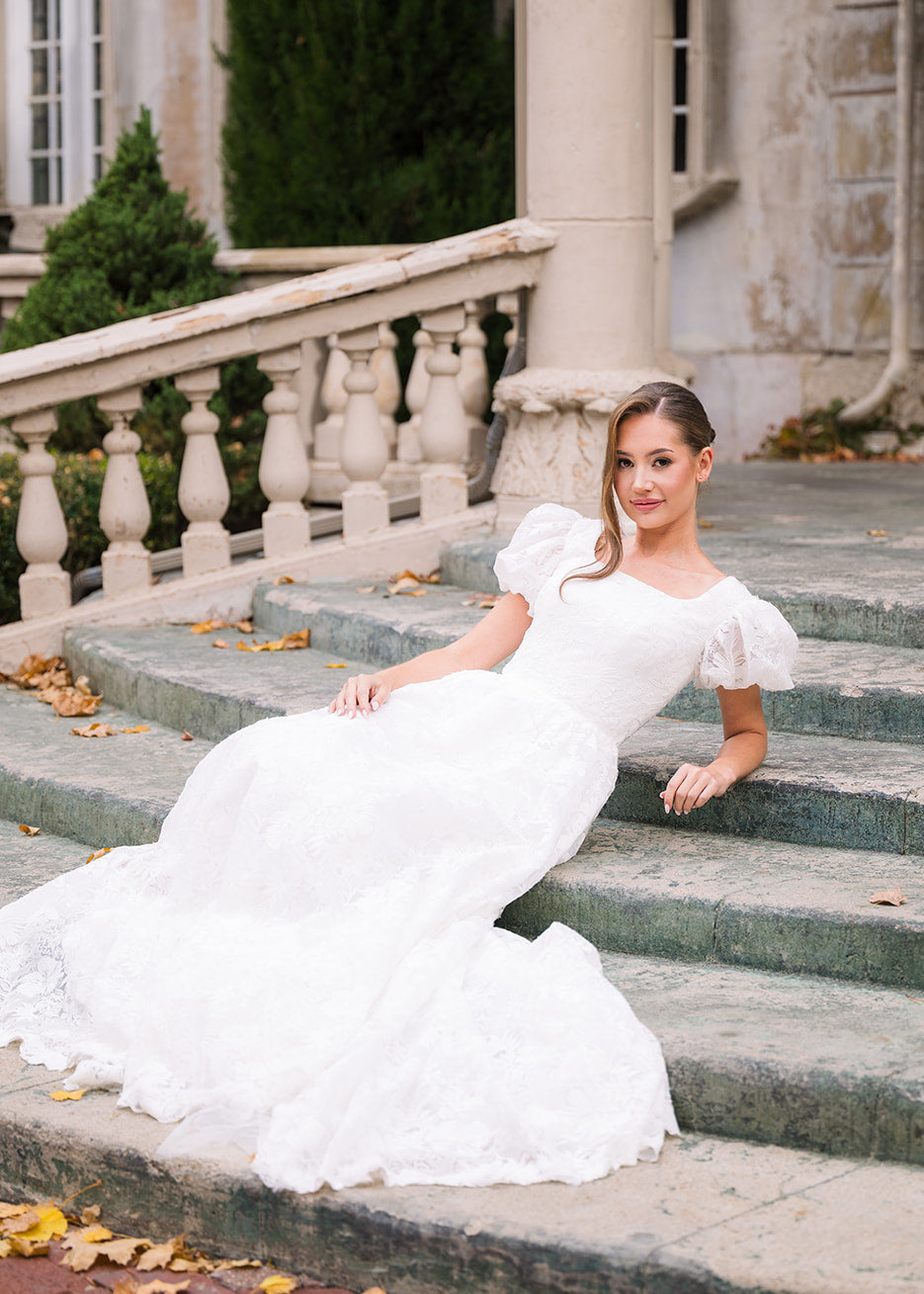 Woman in a white wedding dress sitting on stone steps outdoors.