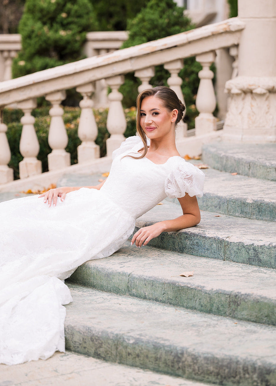 Woman in a white dress sitting on stone steps with classical architecture in the background