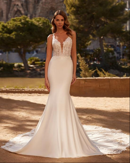 Woman in a white wedding dress standing in front of a large architectural structure with trees in the background.